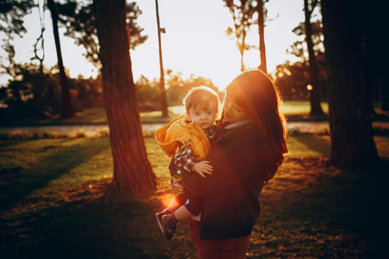 a woman holding a child in her arms, by Matt Stewart, unsplash, taken at golden hour, at a park, avatar image, high quality upload