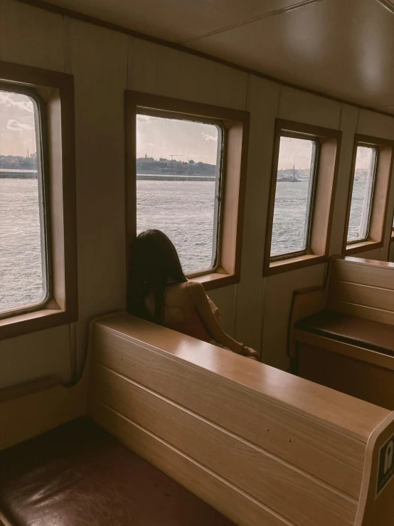 a woman sitting on a bench looking out a window, inspired by Elsa Bleda, unsplash, on liberty island, on a boat, 🚿🗝📝, tumblr aesthetic