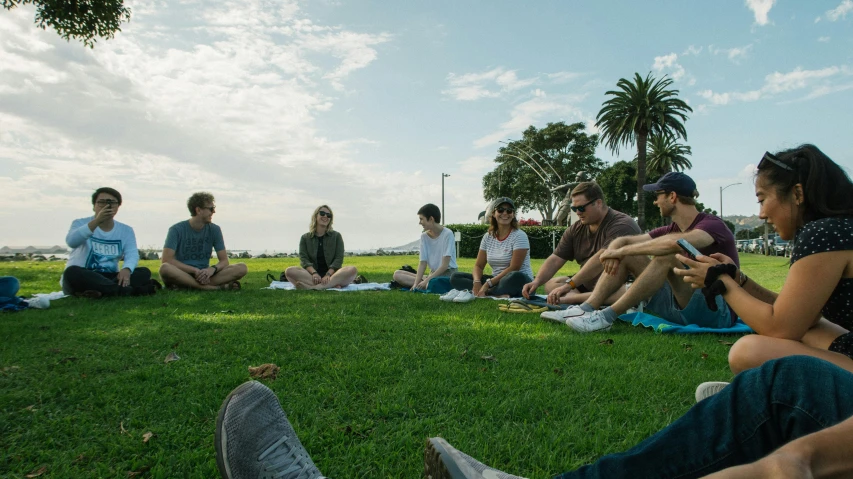 a group of people sitting on top of a lush green field, near the beach, connection rituals, the city of santa barbara, full team