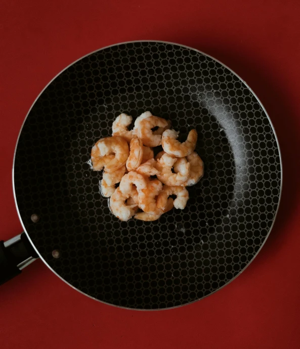 a frying pan filled with shrimp on top of a red table, by Carey Morris, pexels contest winner, food particles, real porcelain texture effect, perfect symmetrical image, with a black background