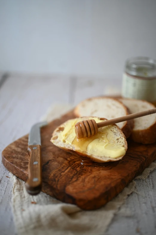 a wooden cutting board topped with bread and butter, unsplash, jar of honey, high quality photo, molten, white