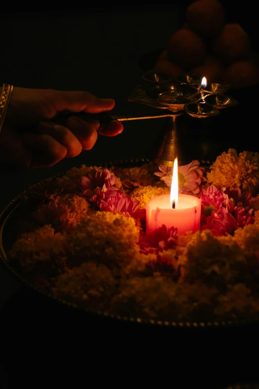 a person lighting a candle in a bowl of flowers, hindu ornaments, dramatic ligthting, pouring, taken in the early 2020s