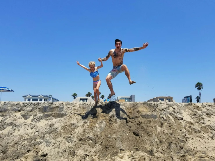 a man and a little girl jumping in the air, by Ryan Pancoast, happening, sand piled in corners, oceanside, of a shirtless, on top of it