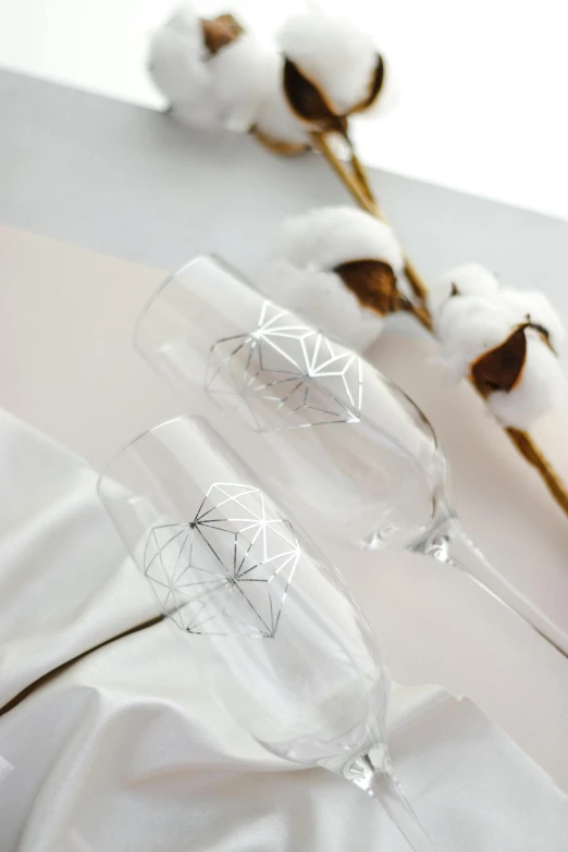 a couple of wine glasses sitting on top of a table, an engraving, inspired by Buckminster Fuller, crystal cubism, sparkling petals, official product photo, with silver runes on it, minimal geometric