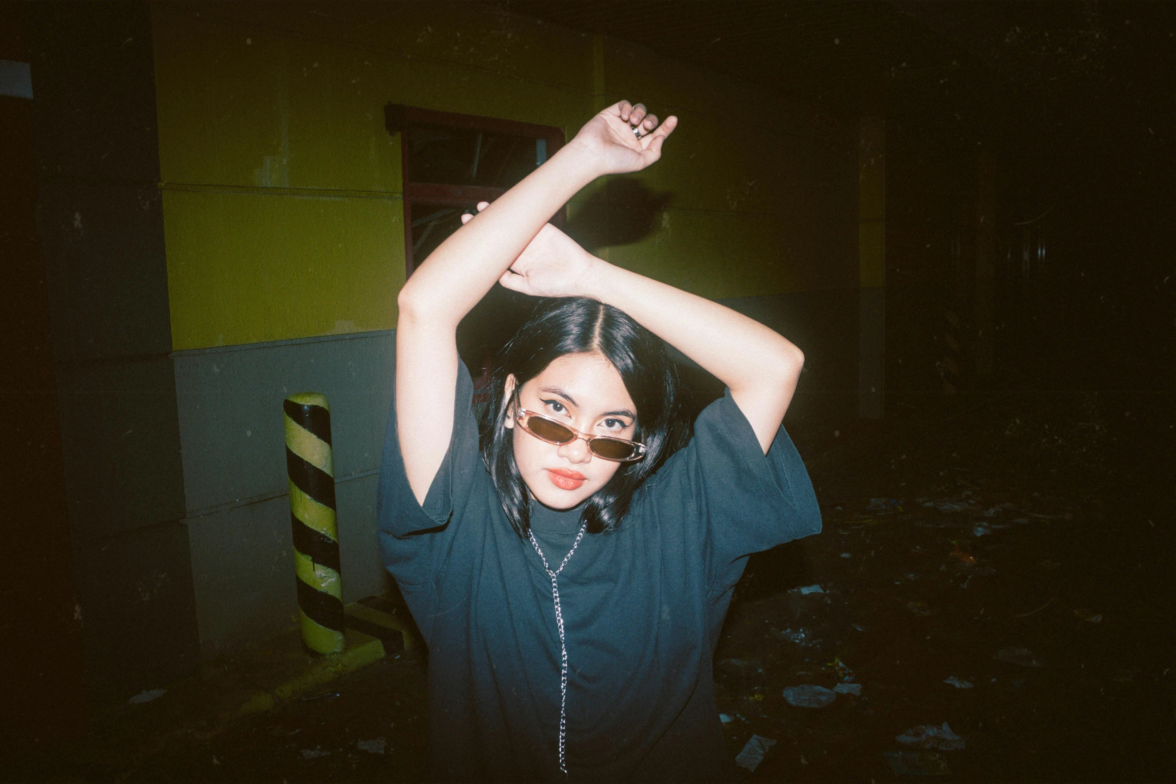 a woman posing for a picture in a dark room, a polaroid photo, inspired by Elsa Bleda, trending on pexels, graffiti, charli xcx, wearing shades, with arms up, sui ishida with black hair