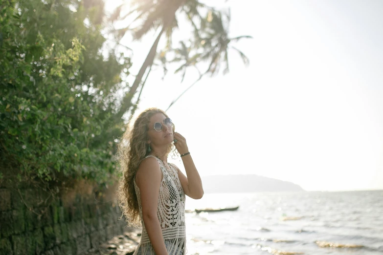a woman standing on a beach next to a body of water, a picture, beyonce photoshoot, profile image, on an island, harsh sunlight