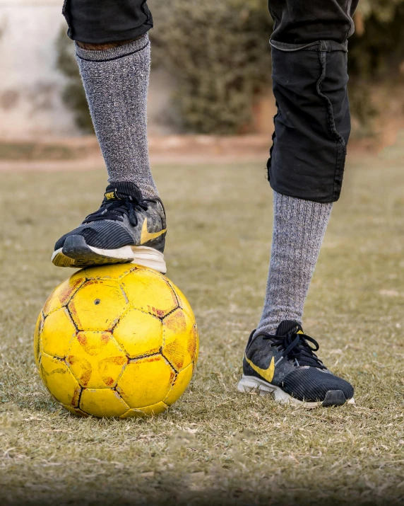 a person standing on top of a yellow soccer ball, gray shorts and black socks, zoomed out, playing, 2019 trending photo