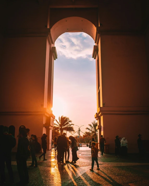 a group of people standing in front of a building, by Alejandro Obregón, pexels contest winner, happening, an archway, nice sunset, with palm trees in the back, portal opening