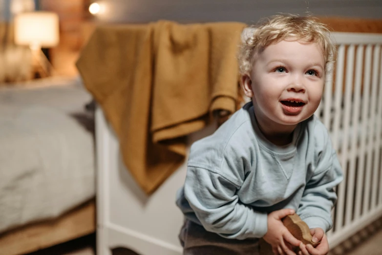 a little boy standing in front of a crib, pexels contest winner, being delighted and cheerful, lights on, curly blonde hair | d & d, very calm and wholesome