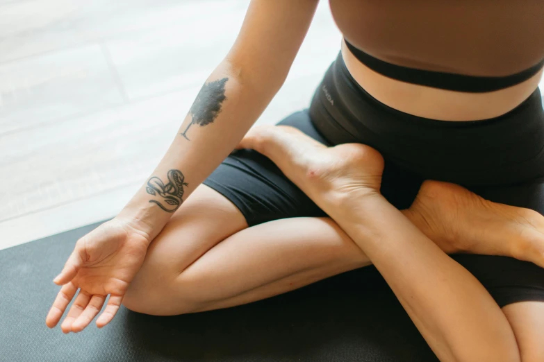 a woman sitting on top of a yoga mat, a tattoo, unsplash, woman holding another woman, from the elbow, manuka, pixeled stretching