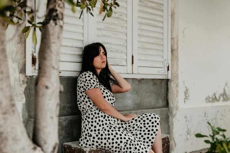 a woman sitting on a bench next to a tree, pexels contest winner, happening, white with black spots, leaning on door, polkadots, profile image