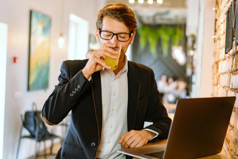 a man sitting in front of a laptop drinking a beverage, a screenshot, by Nicolette Macnamara, pexels, renaissance, wearing a suit and glasses, aussie baristas, moringa juice, energy drink