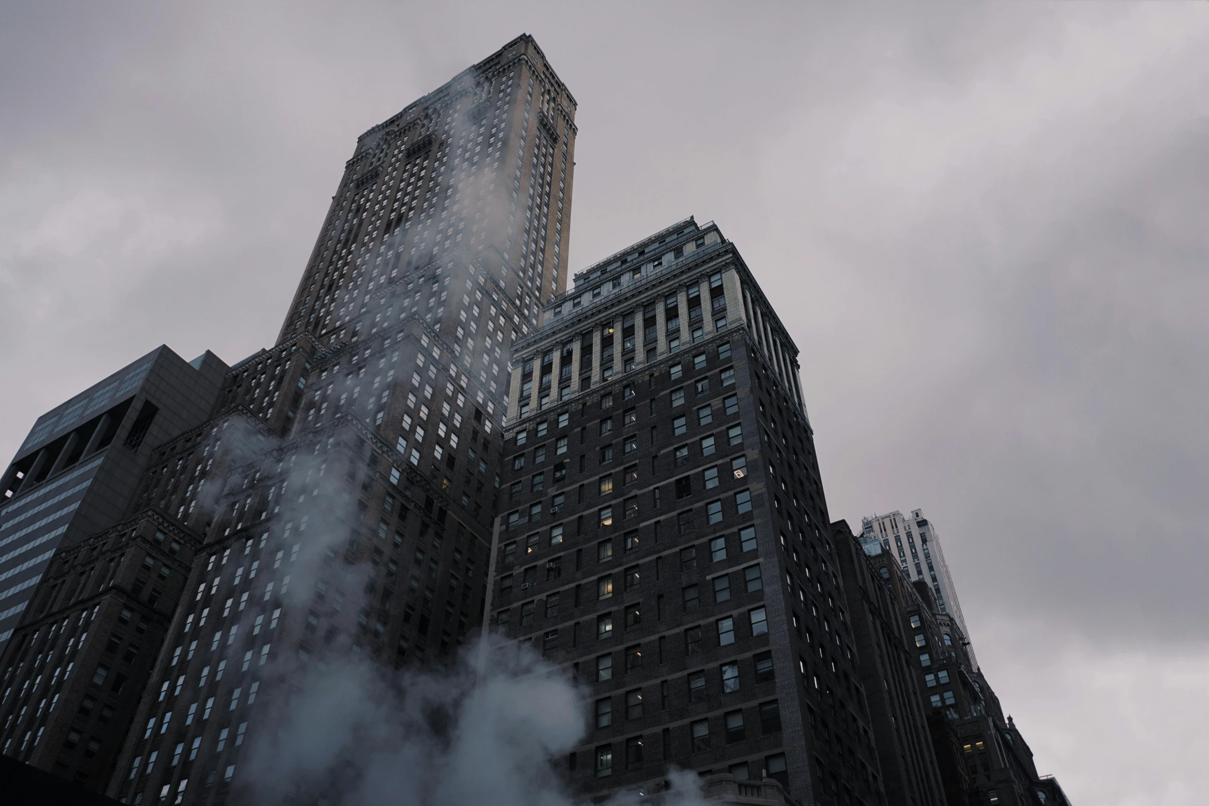 a very tall building with a lot of smoke coming out of it, by Adam Rex, pexels contest winner, new york buildings, spooky fog, low-angle, grey skies