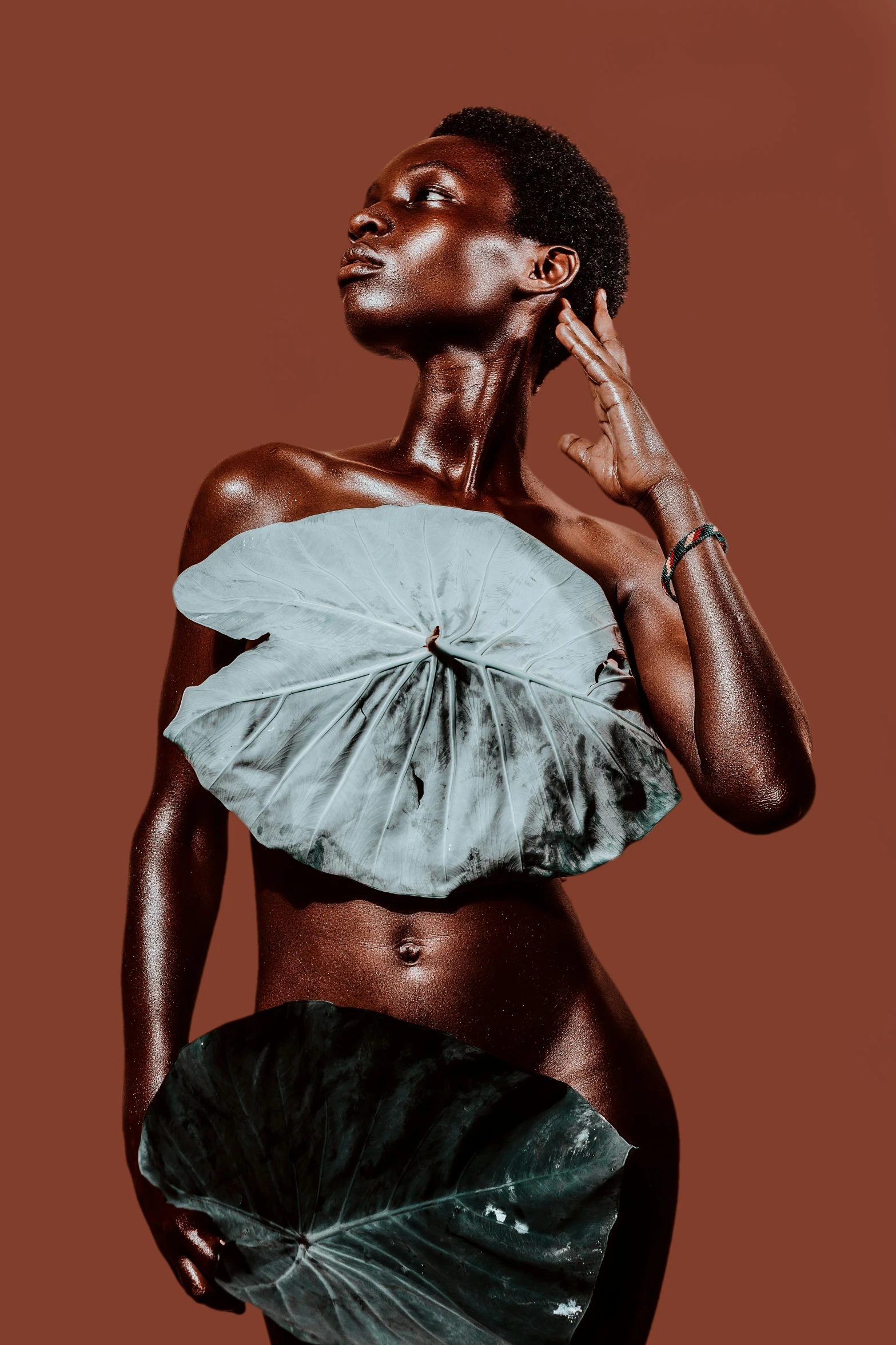 a woman standing in front of a brown background, by Chinwe Chukwuogo-Roy, trending on pexels, afrofuturism, big leaf bra, grey skinned, made of silk paper, physical : tinyest midriff ever