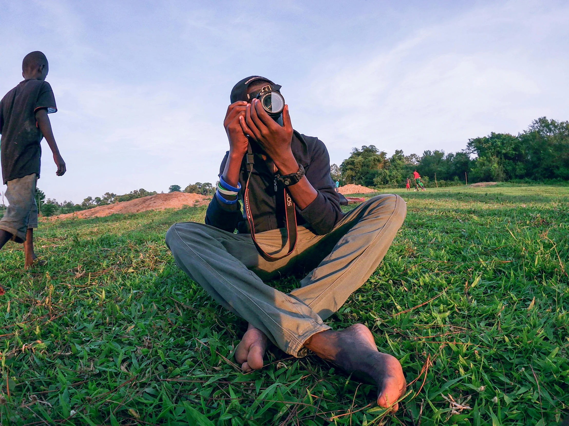 a man sitting in the grass taking a picture with a camera, inspired by Steve McCurry, pexels contest winner, mohamed chahin style, afar, wide angle full body, medium format