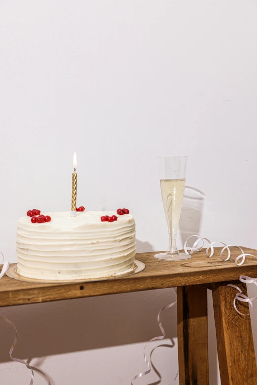 a white cake sitting on top of a wooden table, a still life, by Nicolette Macnamara, trending on unsplash, drinking champagne, set against a white background, happy birthday candles, crimson themed