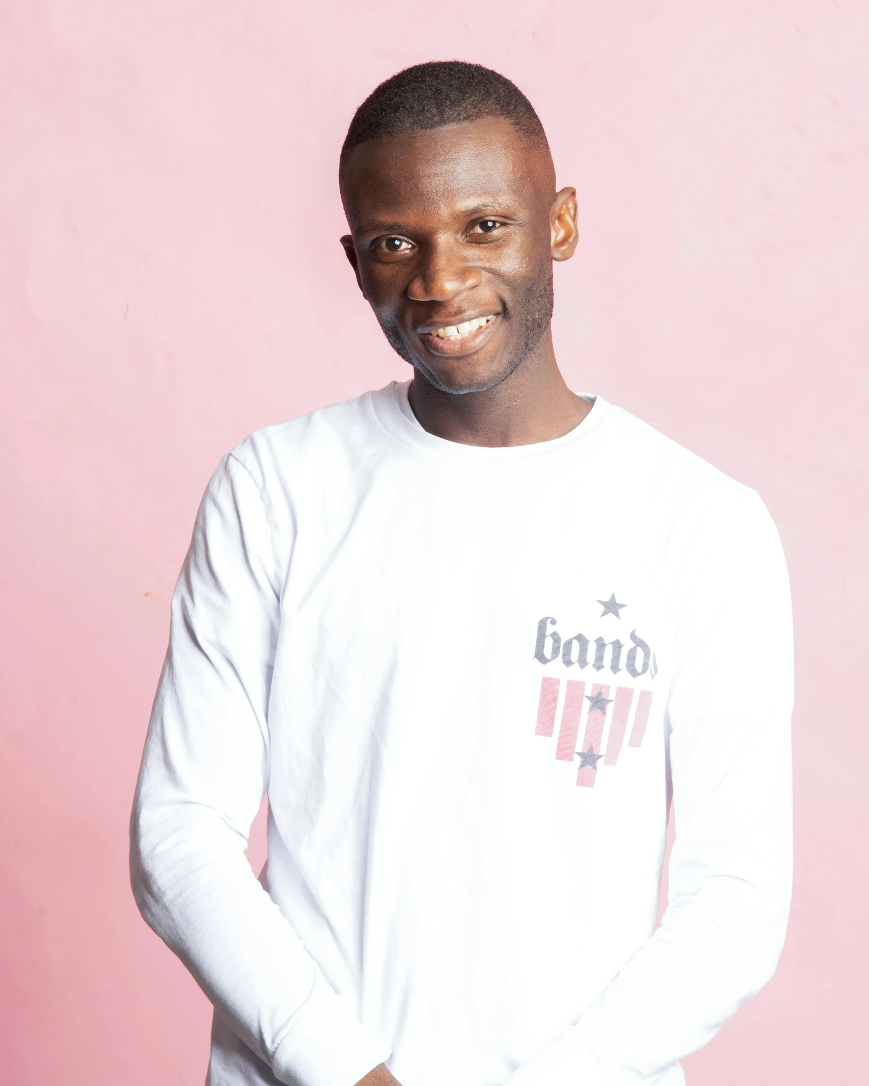 a man standing in front of a pink wall, an album cover, inspired by Camille-Pierre Pambu Bodo, wearing stripe shirt, wearing presidential band, white t-shirt, adut akech