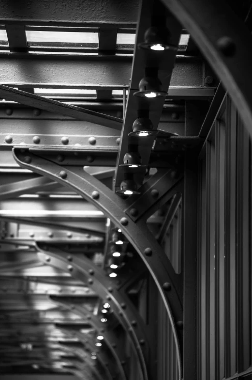 a black and white photo of the underside of a bridge, inspired by Brassaï, rivets, lights inside, wrought iron, vivid)