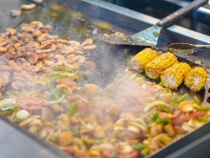 a pan filled with food cooking on top of a stove, food court, corn, shrimp, blowing out smoke