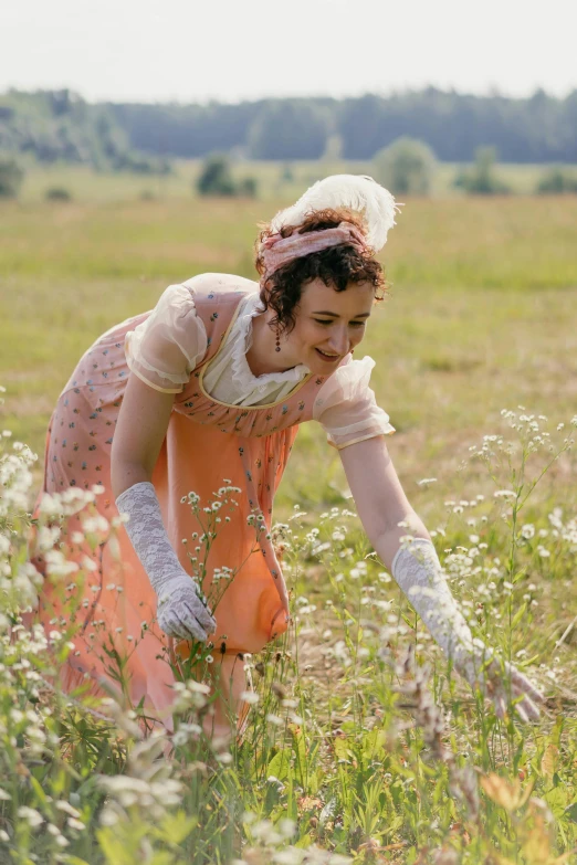 a woman in an orange dress in a field, inspired by Cassandra Austen, picking up a flower, movie still, square, regency-era