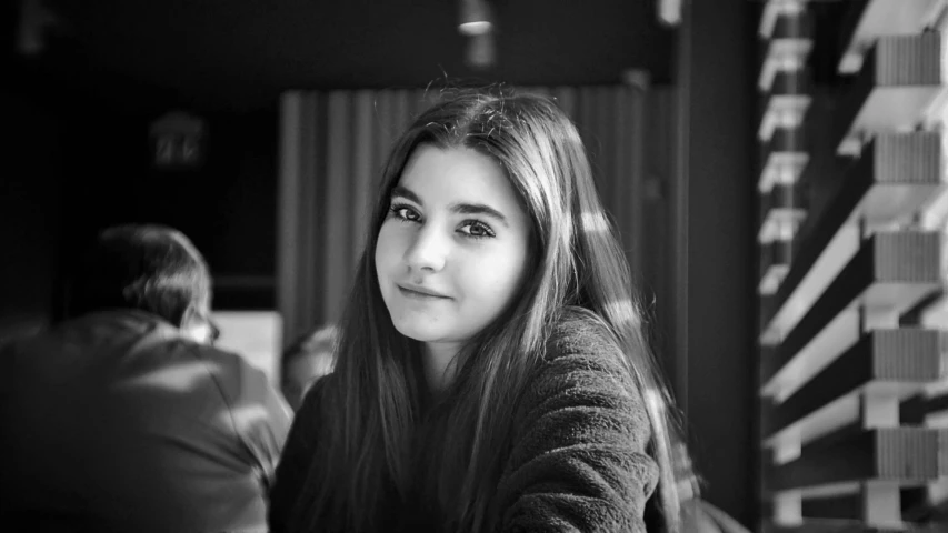 a black and white photo of a woman sitting at a table, a black and white photo, pixabay, hurufiyya, dslr photo of a pretty teen girl, 🤤 girl portrait, headshot profile picture, warm smile