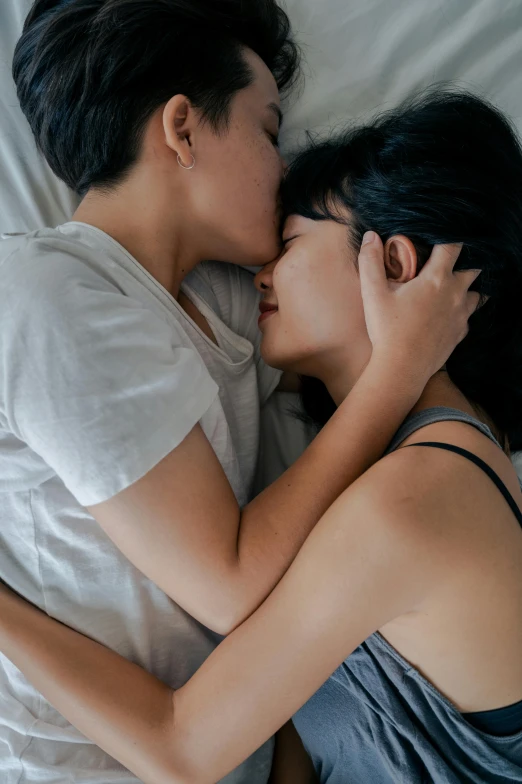 a man and woman laying in bed next to each other, inspired by Nan Goldin, unsplash, lesbian kiss, asian woman, high angle, grey