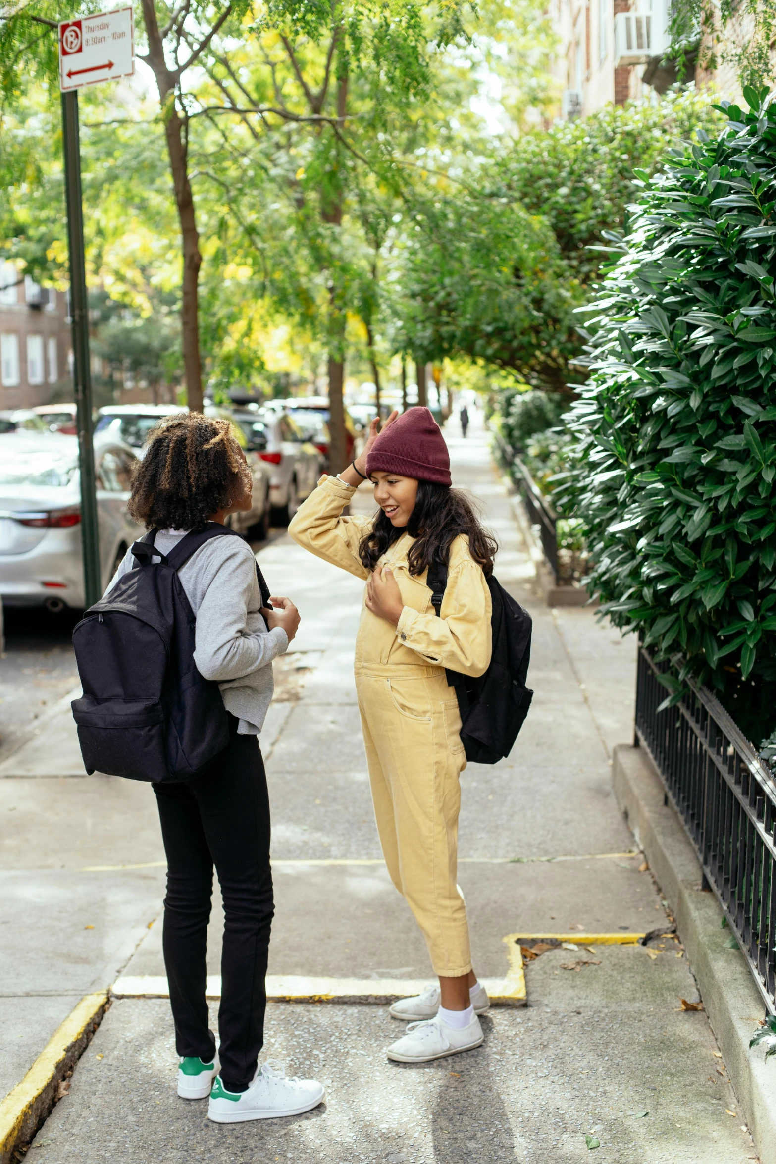 a couple of women standing next to each other on a sidewalk, by Nina Hamnett, happening, with a backpack, yellow clothes, talking, wearing a hoodie and sweatpants