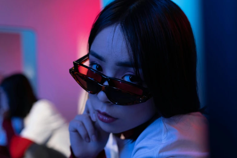 a woman wearing sunglasses sitting in front of a mirror, inspired by Elsa Bleda, unsplash contest winner, blue and red lights, young asian girl, photograph of a techwear woman, avatar image