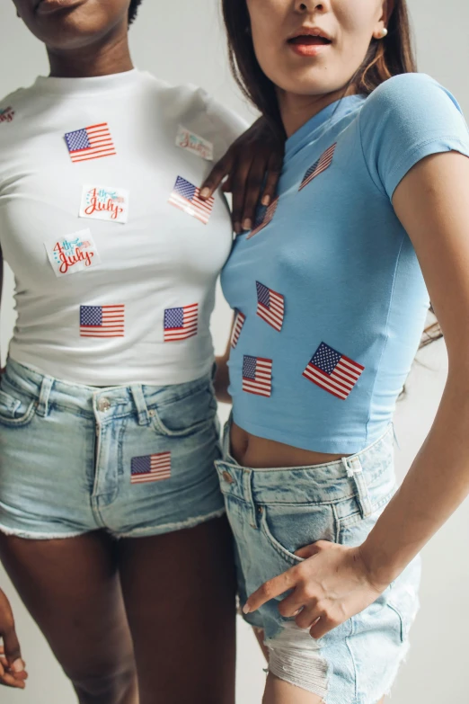 a couple of women standing next to each other, by John Luke, american flags, with ripped crop t - shirt, puffy sticker, detail shot