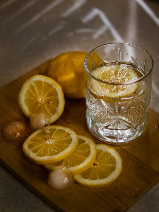 a wooden cutting board topped with sliced lemons, a still life, by Leo Michelson, pexels contest winner, renaissance, drinking, promo image, crystal water, nightcap