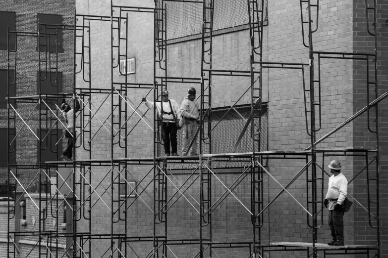 a group of men standing on scaffolding in front of a building, pexels, constructivism, inside a frame on a tiled wall, 70s photo, mesh structure, brick building