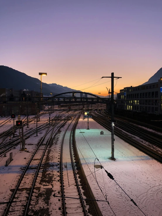 a train traveling down train tracks next to a mountain, by Karl Stauffer-Bern, unsplash contest winner, twilight in the city, cold snowy, photo on iphone, station