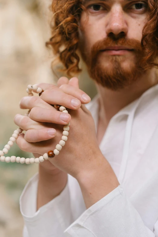 a close up of a person holding a rosary, by Dan Content, unsplash, renaissance, braided beard redhead dreadlocks, wearing white clothes, anjali mudra, adam ondra