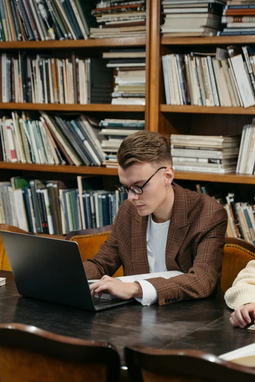 a couple of people sitting at a table with a laptop, trending on pexels, academic art, grand library, vitalik buterin, academic clothing, non binary model