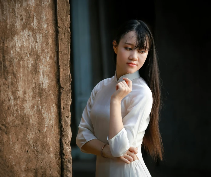 a woman in a white dress leaning against a wall, inspired by Cui Bai, pexels contest winner, realism, ao dai, 15081959 21121991 01012000 4k, wearing a light shirt, pale thin lips