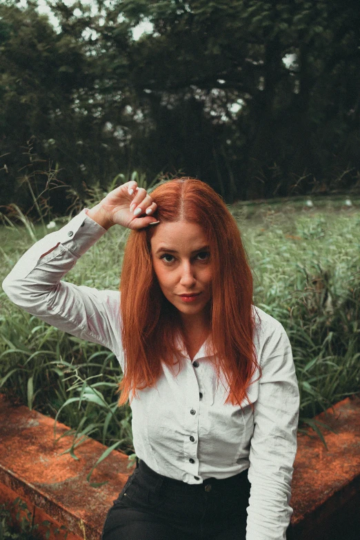 a woman with red hair sitting on a bench, an album cover, inspired by Elsa Bleda, pexels contest winner, wearing a white button up shirt, hands in her hair, orange hue, standing in a botanical garden