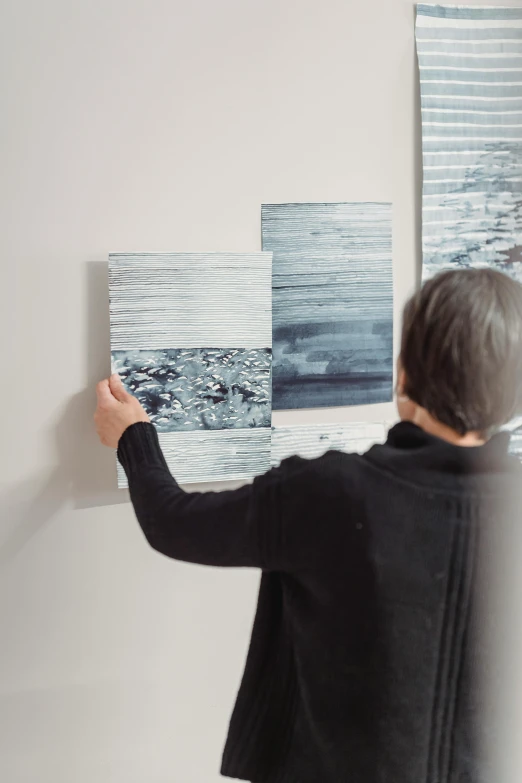 a woman standing in front of a painting on a wall, a photorealistic painting, inspired by Richter, trending on unsplash, white grey blue color palette, close-up print of fractured, gallery display photograph, seaside