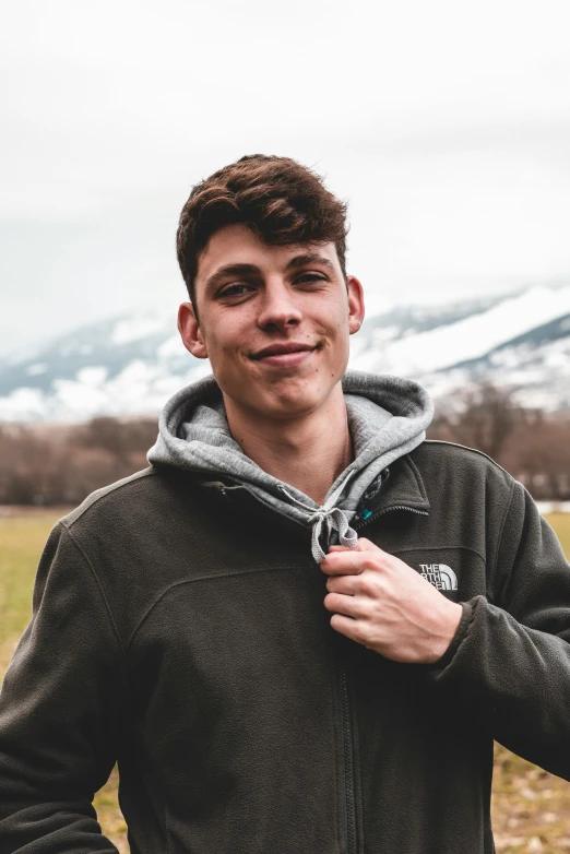 a man standing in a field with mountains in the background, inspired by John Luke, discord profile picture, headshot profile picture, teddy fresh, kailee mandel