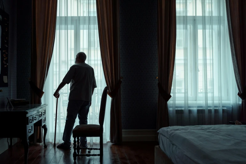 a man standing in front of a curtained window with a cane