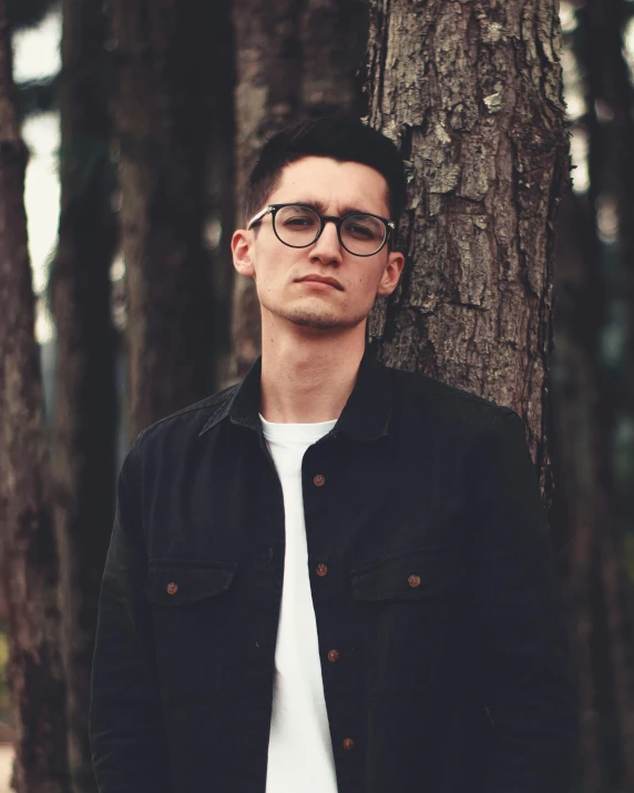 a young man is leaning against a tree