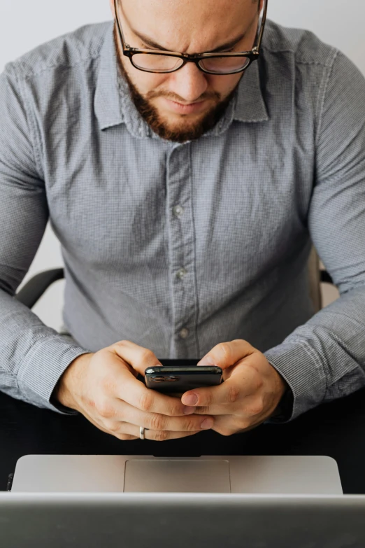 a man sitting at a table looking at his cell phone, trending on pexels, gray shirt, corporate phone app icon, holding arms on holsters, bearded