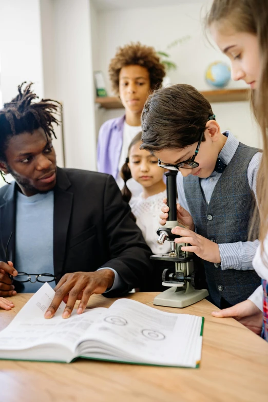 a group of people sitting around a table looking at a book, trending on pexels, paris school, microscope, black teenage boy, with a lab coat, teacher