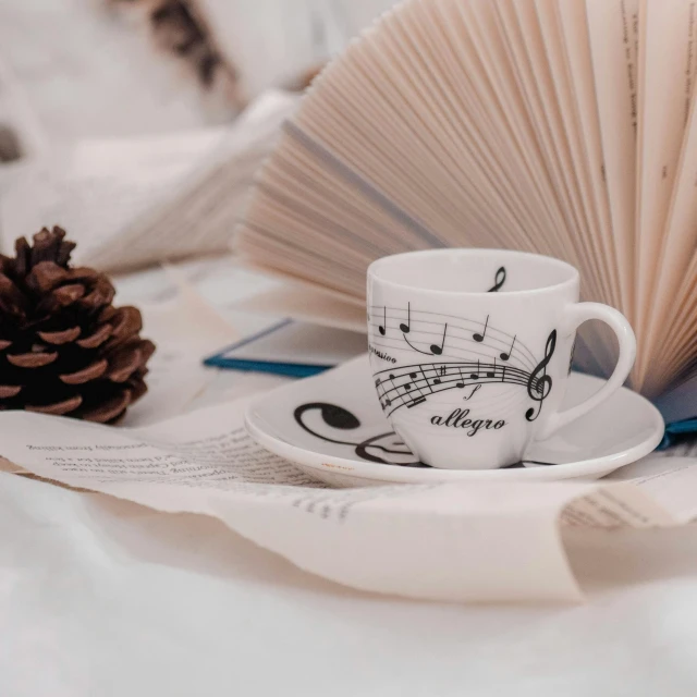 a book sitting on top of a bed next to a cup and saucer, an album cover, by Lucia Peka, pexels contest winner, music notes, white mug, wintertime, nightcore