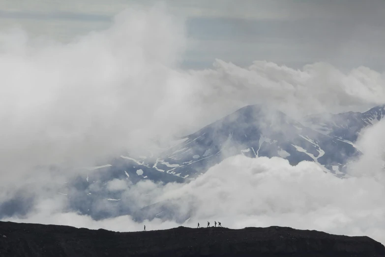 a lone man sitting on top of a mountain looking at the clouds