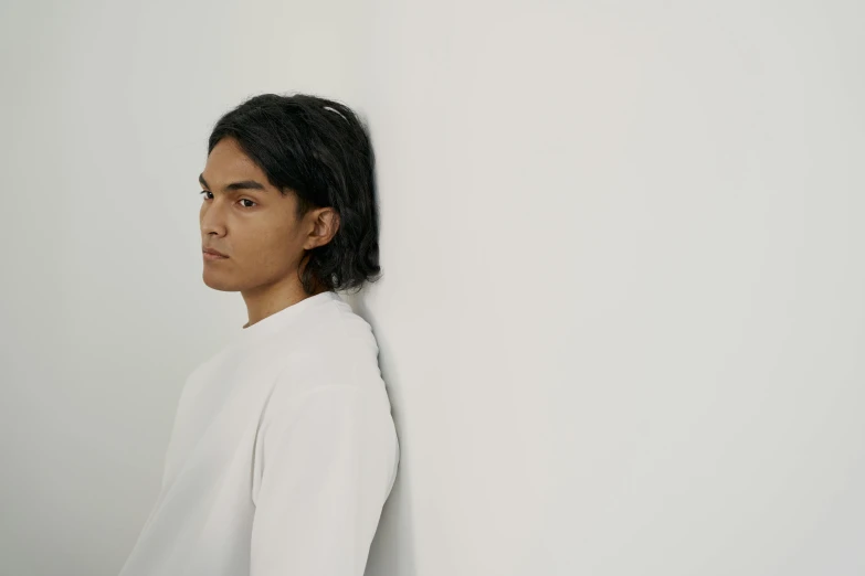 a man in a white shirt leaning against a wall, an album cover, inspired by Jorge Jacinto, wearing a white sweater, profile view, ignant, shoulder - length hair