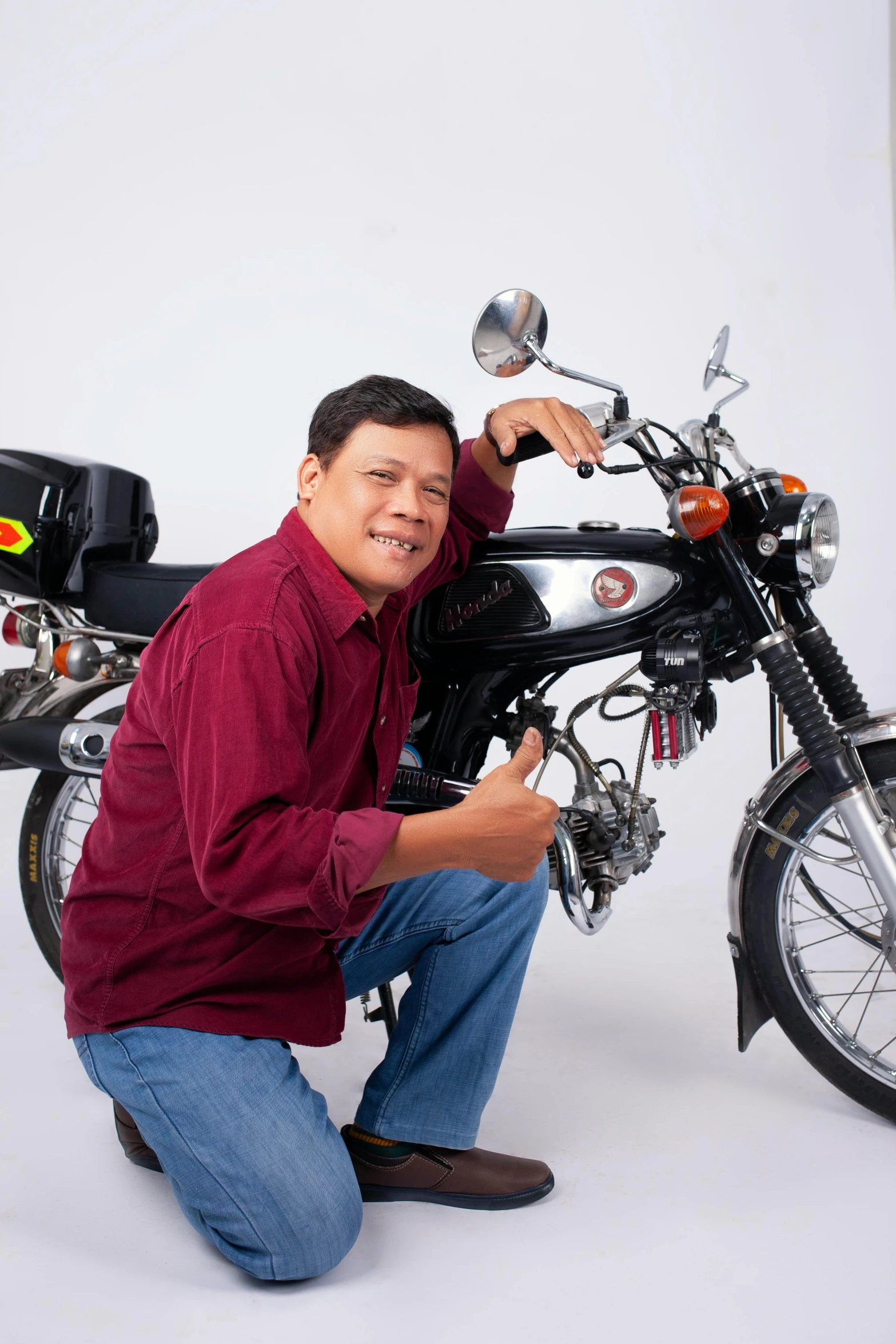 a man with a red shirt on kneeling next to a motorcycle