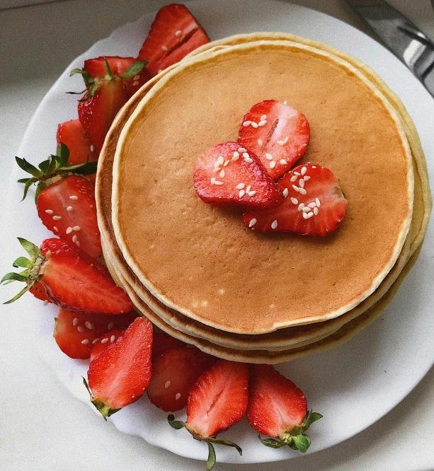 a stack of pancakes on a plate with strawberries on top