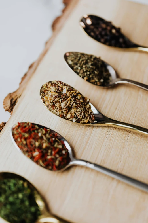 a group of spoons sitting on top of a wooden board, dried herbs, infused, detailed product image, opening shot