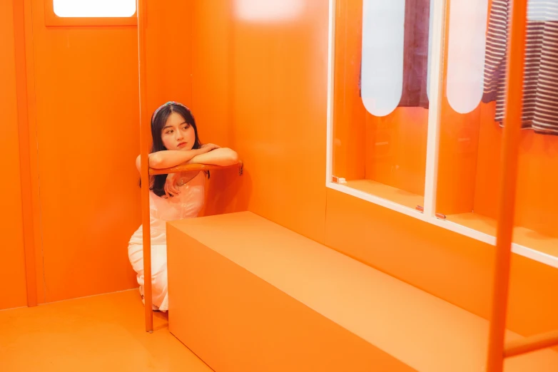 a woman sitting on a bench in an orange room, inspired by Cheng Jiasui, unsplash, interactive art, capsule hotel, square, ulzzang, in white room