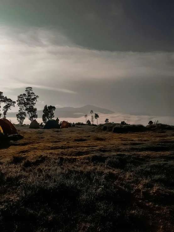 a couple of tents sitting on top of a grass covered field, fog and dirt, taken on iphone 1 3 pro, high-quality photo, black volcano afar